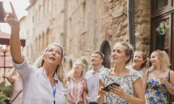Medium group of people standing in a street in Volterra. They're listening to a tour guide who is talking about the architecture and the history.